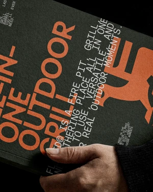 Hand holding a dark textured booklet with bold orange typography and maker's mark graphic for Flamid brand identity.