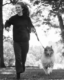 Model in dark sweater walking a collie dog outdoors in a park for Tuckernuck High Fall campaign.