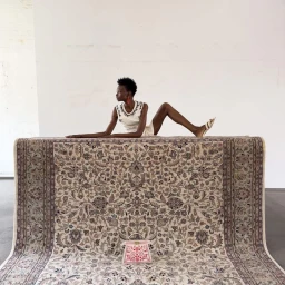 Model lying on a large patterned rug against a plain white wall for Numéro Berlin, photographed by Daniel Roché.