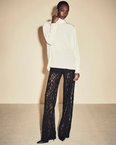 Model wearing a white high-neck blouse and black lace trousers against a neutral background for FRAME.