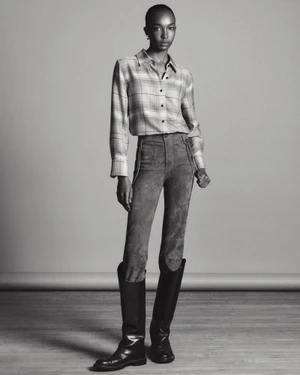 Model in plaid shirt and dark trousers wearing knee-high boots against a grey studio backdrop