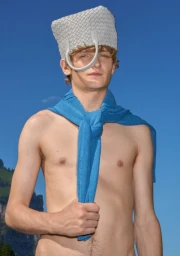 Shirtless young man wearing a grey woven handbag as a hat and a blue knitted sweater tied around his neck