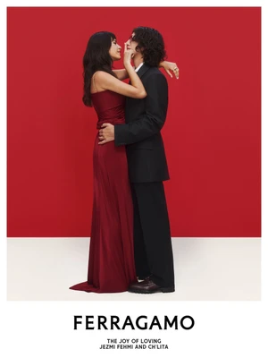 Ferragamo campaign image of a woman in a long red dress embracing a man in a black suit against a red and white backdrop