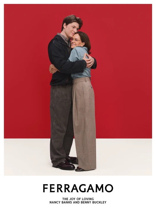 Two people embracing against a solid red backdrop with a white floor featuring the Ferragamo logo and text below.