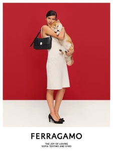 Woman in a white dress holding a dog and a black handbag against a red and cream background