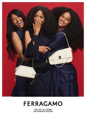 Three smiling women in dark navy blue dresses holding white leather handbags against a solid red background