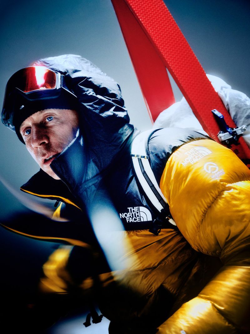 Man wearing a yellow and black puffer jacket with ski goggles and skis for The North Face Summit Nuptse campaign.