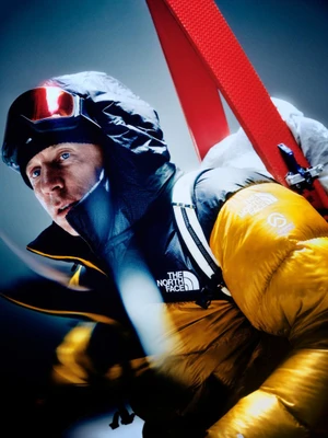 Man wearing a yellow and black puffer jacket with ski goggles and skis for The North Face Summit Nuptse campaign.