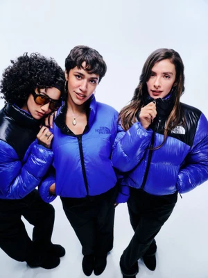 Three female models wearing blue and black puffer jackets against a plain white studio background.