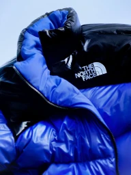 Close up of a blue and black puffer jacket featuring The North Face logo embroidered on the chest against a pale background