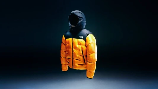 The North Face yellow and black puffer jacket displayed on a dark gradient background with dramatic lighting