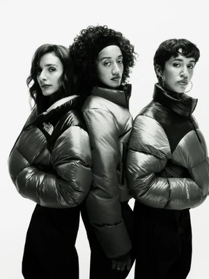 Three female models wearing black and silver puffer jackets posing against a solid white background.