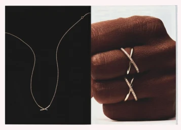 Close-up of diamond pavé crossover rings worn on fingers alongside a delicate chain necklace on black