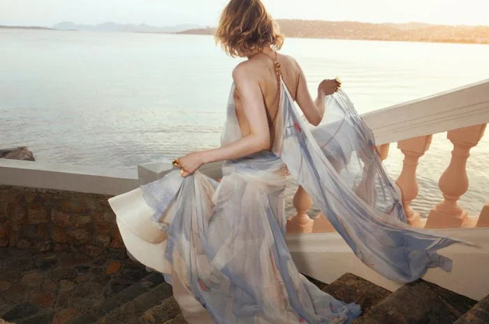 Model Aivita Muze in a flowing printed dress descending stone stairs by the ocean for Zimmermann