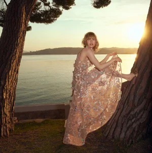 Model in sheer embroidered dress climbing a tree by the water at sunset