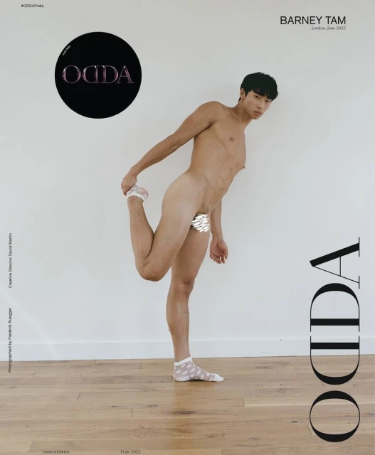 Shirtless person in socks poses, stretching with leg up against white wall and light wood floor in studio. Fashion photography.