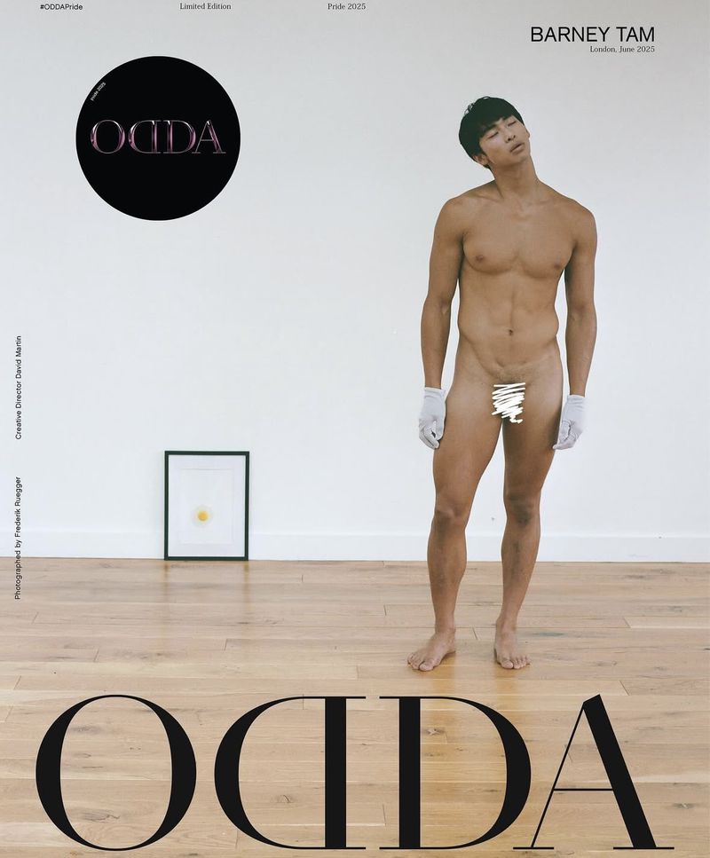 Nude adult male model wearing gloves poses in a photo studio against a white wall with hardwood floor. Fashion editorial shot. 