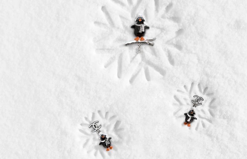 Three penguin-themed luxury jewellery pieces arranged on a textured white snowfield with snowflake impressions.