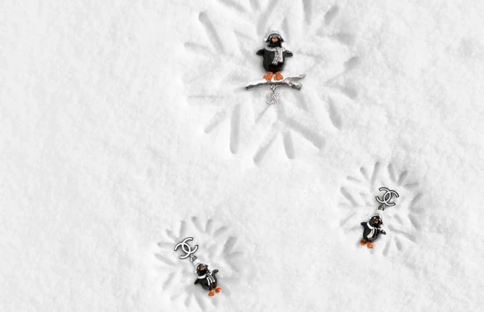 Three penguin-themed luxury jewellery pieces arranged on a textured white snowfield with snowflake impressions.