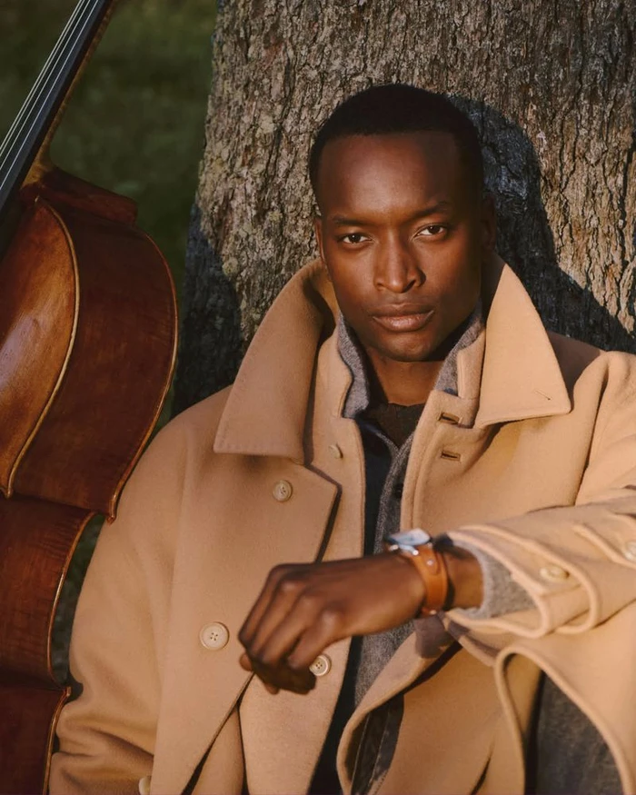 Model in camel coat leaning against a tree trunk next to a cello for Ralph Lauren Fall Holiday 2026 Campaign