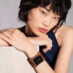 Close-up portrait of model Wenli Zhao wearing a brown leather Apple Watch band for Hermes against a neutral grey studio background