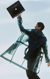 Model holding a black leather briefcase aloft wearing a translucent green raincoat against a clear sky.