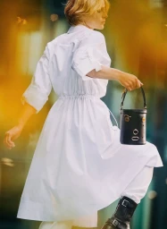 Model wearing a white dress and black bucket bag with gold hardware for Hermès Arts & Facts