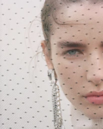 Close-up portrait of a woman looking through a dotted veil wearing dangling rhinestone earrings for H&M Studio AW 2026
