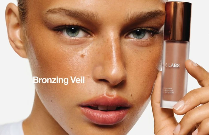 Close-up beauty portrait of a model holding a Haus Labs bronzer bottle against a plain white background