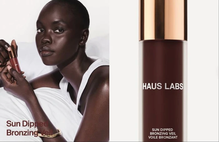 Model holding bronzer bottle wearing white tank top against white background for Haus Labs Bronzing Veil campaign