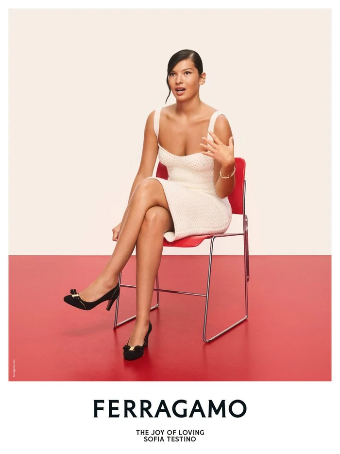 Sofia Testino seated on a red chair wearing a white dress and black heels for Ferragamo Holiday 2026