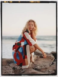 Blonde model crouching on coastal rocks wearing a patterned robe for InStyle Mexico