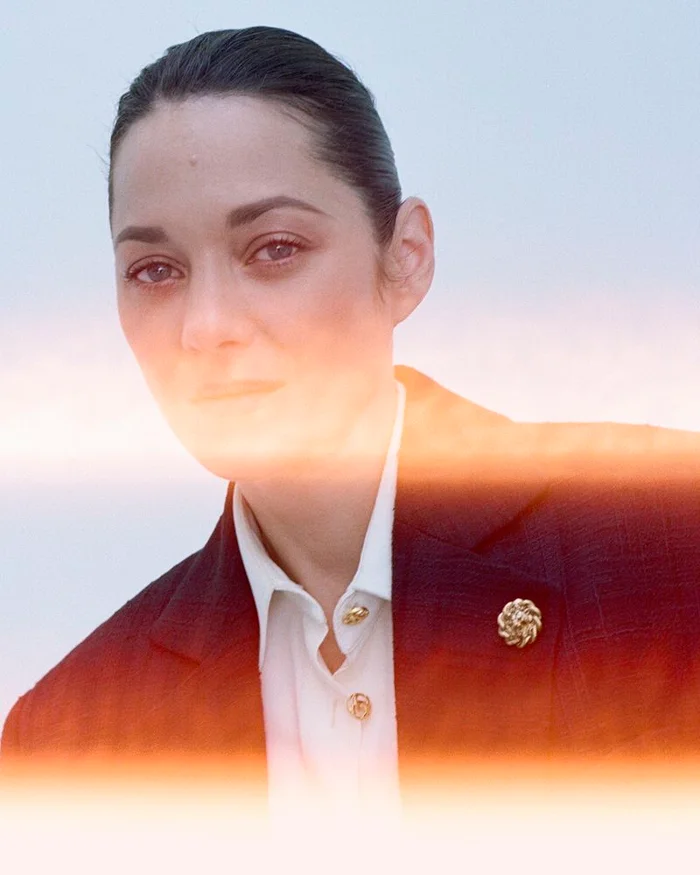 Portrait of actress Marion Cotillard wearing a white shirt and dark blazer with a bright light leak across the center