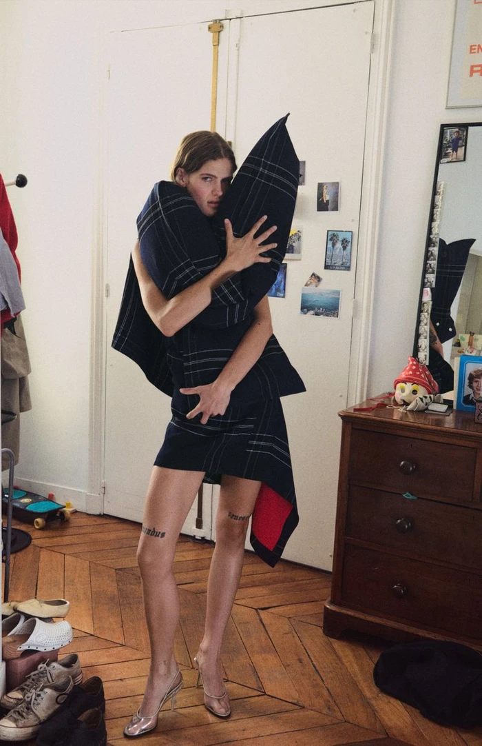 Model hugging a large dark plaid pillow inside a domestic room, captured by photographer Oliver Hadlee Pearch for Crosscurrent.