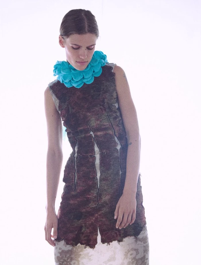 Model in a textured dark dress with a bright turquoise ruffled collar against a bright white background