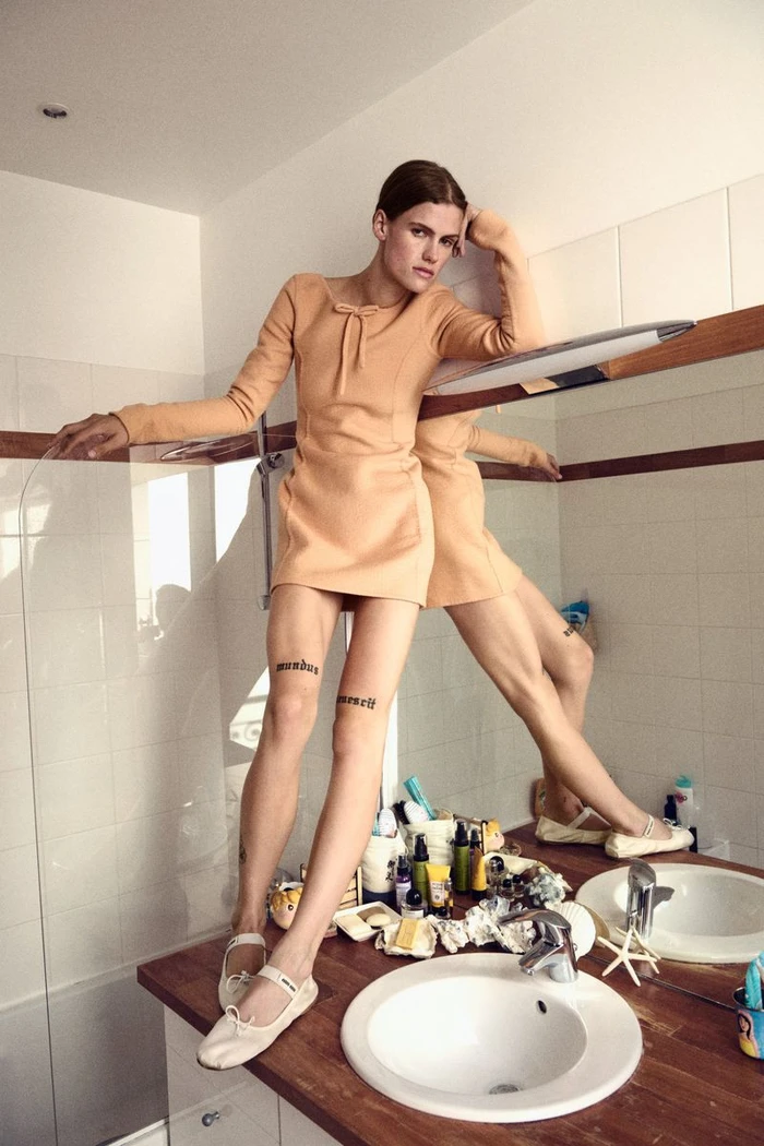 Model wearing a peach mini dress and white ballet flats standing on a bathroom vanity