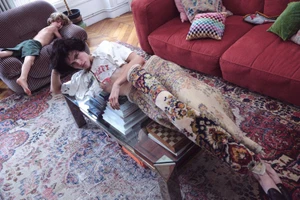 Model lying on glass coffee table in domestic interior with red sofa and ornate rug