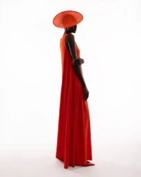 Model wearing a vibrant red floor length dress and matching wide brim hat against a bright white background