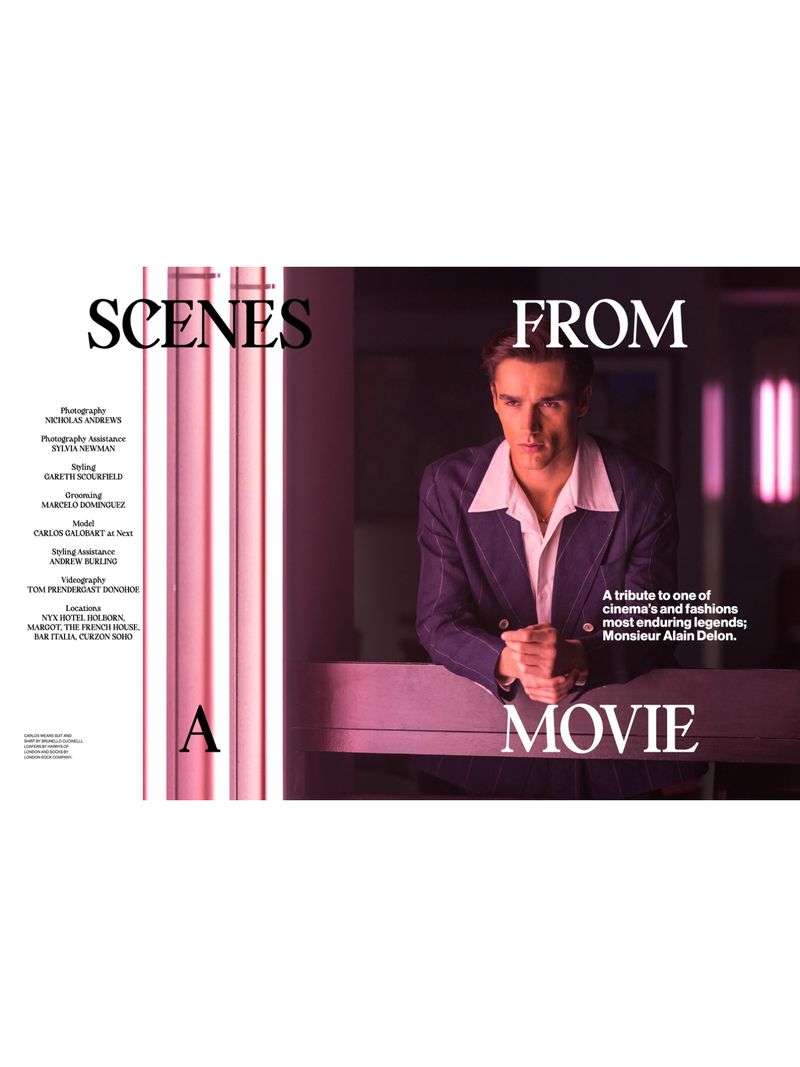 A man in a suit jacket stands near a railing indoors with pink lighting, in a scene referencing cinema and fashion history.