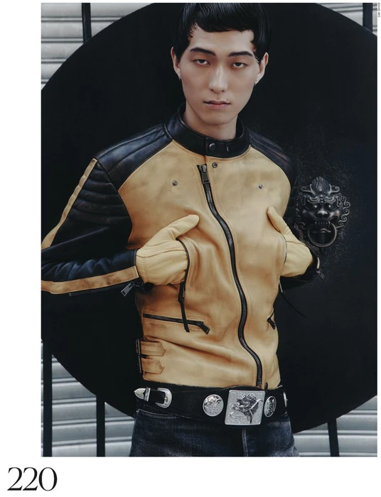 Model wearing yellow and black leather jacket with matching gloves against dark round backdrop