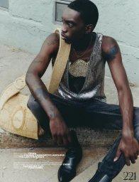 Black man seated on pavement wearing sequin tank top and dark jeans with large straw shoulder bag