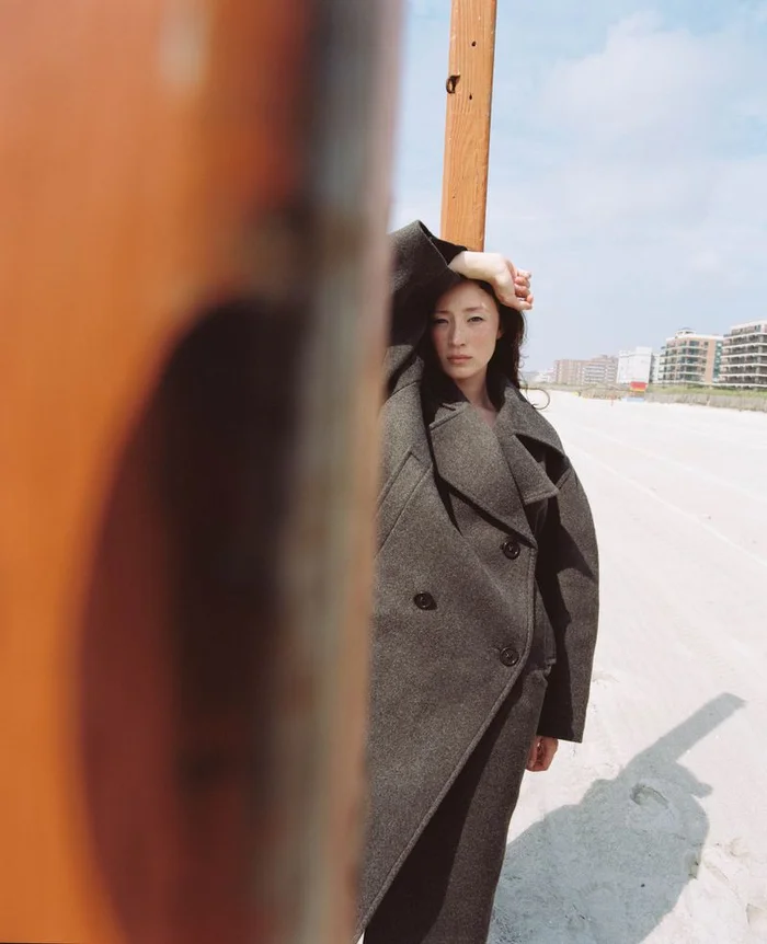 Havana Rose Liu wearing a dark grey coat on a beach for Flaunt, photographed by Arno Frugier