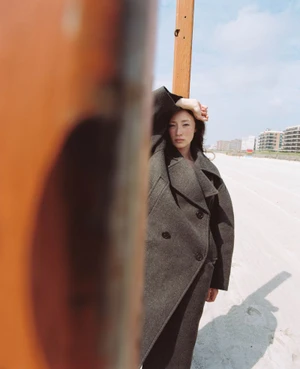 Havana Rose Liu wearing a dark grey coat on a beach for Flaunt, photographed by Arno Frugier