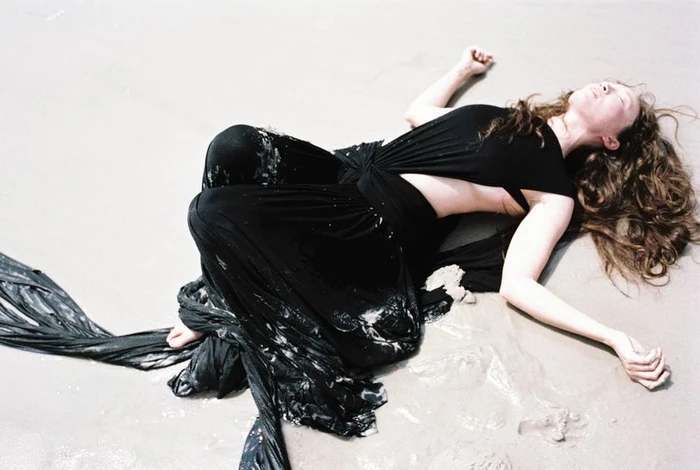 Havana Rose Liu lies on wet sand wearing a flowing black dress, photographed by Arno Frugier for Flaunt.