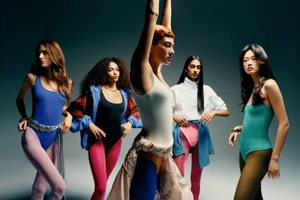 Five models posing in vibrant athletic bodysuits and colorful tights against a dark studio background for V Magazine.