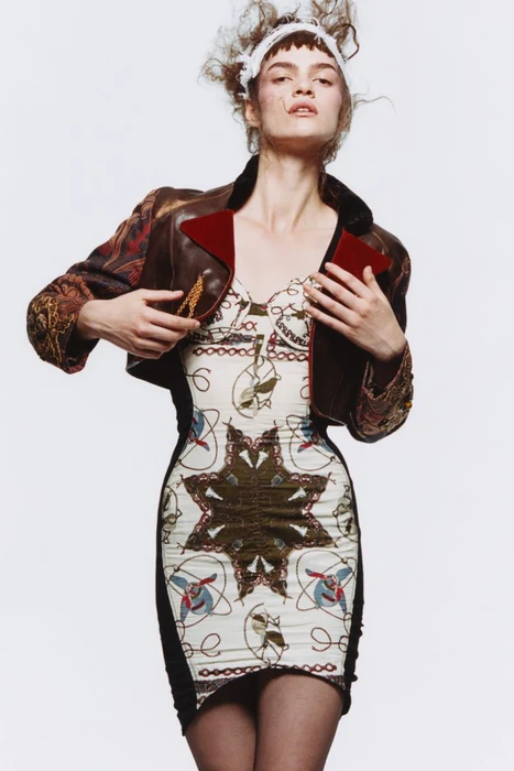 Model in patterned fitted dress and brown cropped jacket against plain white background for System Magazine