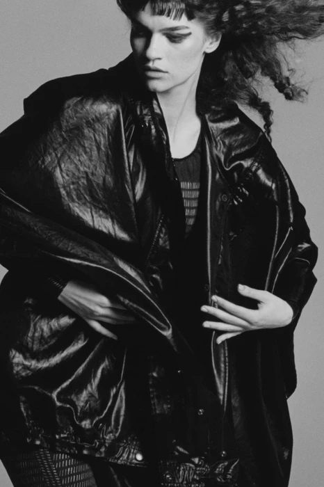 Model in dark leather jacket and textured dark clothing against a plain grey background for System Magazine.