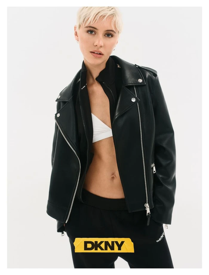 Model Iris Law with short blonde hair wearing a black leather jacket and sweatpants against a white background for DKNY Fall 26
