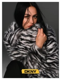 Model Amelia Gray with dark hair wearing a black and white faux fur zebra coat against a grey backdrop for DKNY.