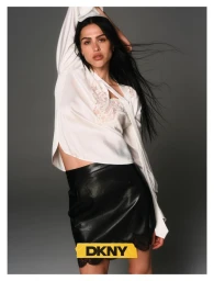 Model with long dark hair wearing a white silk top and black skirt against a grey seamless background